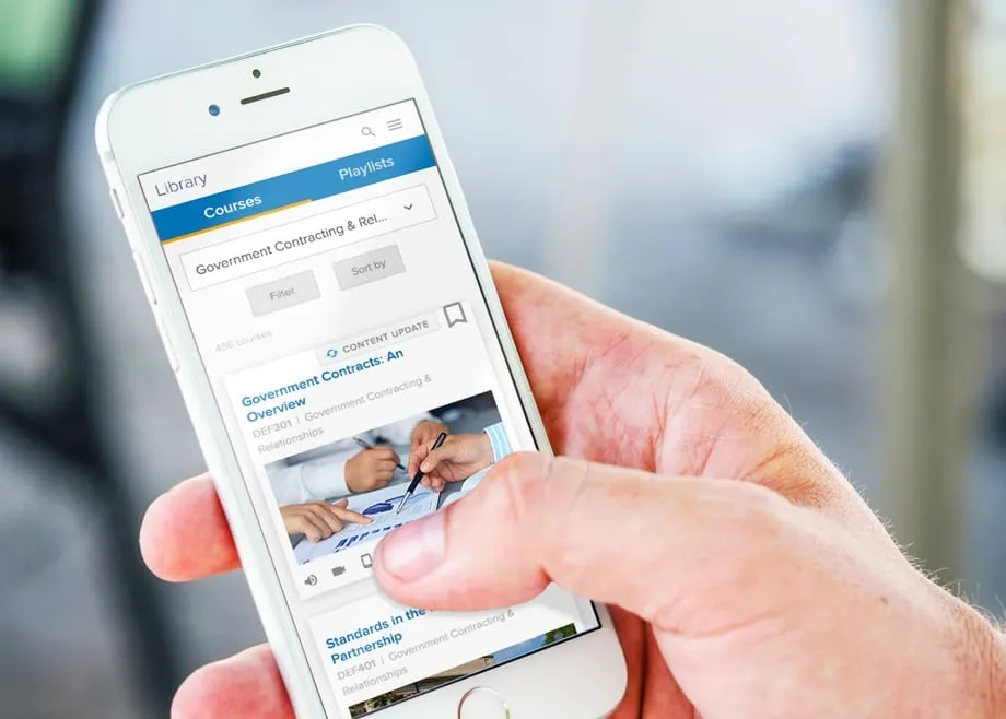 A hand holding a phone showing the training app's library and playlists.